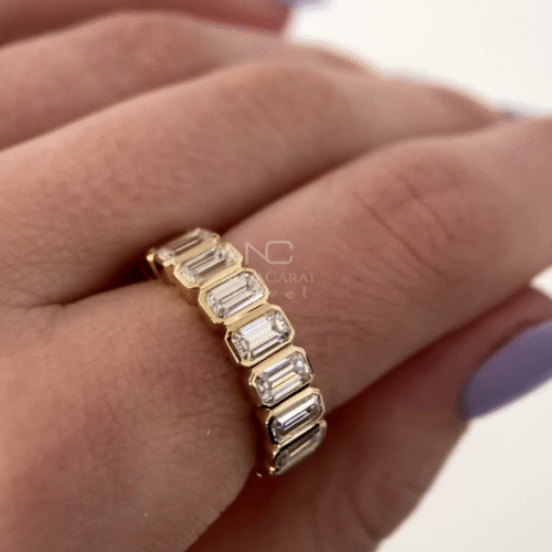 Emerald cut moissanite diamond eternity band worn on hand, bezel set in 14k Yellow gold, stackable bridal band with sparkling moissanite diamonds, perfect for weddings and anniversaries, Emerald Cut Moissanite Diamond Eternity Ring, Bezel Set Emerald Cut Eternity Band, Diamonds Wedding Band, Emerald Cut Moissanite Diamond Half Eternity Band, Bezel Set Promise Anniversary Ring, Unique Stackable Bridesmaid & Wedding Gift for Her, Emerald Cut Moissanite Wedding Band 14K Yellow Gold Wedding Ring