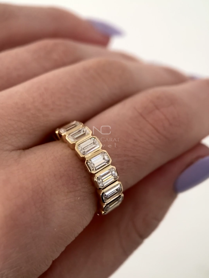Emerald cut moissanite diamond eternity band worn on hand, bezel set in 14k Yellow gold, stackable bridal band with sparkling moissanite diamonds, perfect for weddings and anniversaries, Emerald Cut Moissanite Diamond Eternity Ring, Bezel Set Emerald Cut Eternity Band, Diamonds Wedding Band, Emerald Cut Moissanite Diamond Half Eternity Band, Bezel Set Promise Anniversary Ring, Unique Stackable Bridesmaid & Wedding Gift for Her, Emerald Cut Moissanite Wedding Band 14K Yellow Gold Wedding Ring