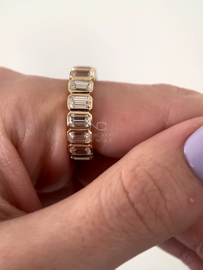Background image of emerald cut moissanite eternity ring, 14k Yellow gold bezel set design, stackable band crafted as a timeless wedding ring and promise band for her. Emerald Cut Moissanite Diamond ring, Bezel Set Emerald Cut Eternity Band, 14K Yellow Gold Wedding Band Stackable Band Emerald Minimalist Band Anniversary Ring, Stackable Bridal Diamond Band, Emerald Moissanite, Promise Ring, Emerald cut moissanite eternity band in 14k Yellow gold, Bezel set minimalist stacking ring, perfect bridal