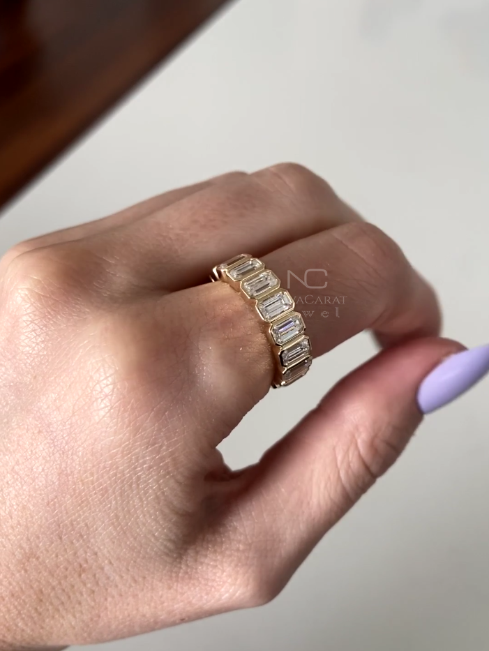 Close up of emerald cut moissanite eternity ring, bezel set in Yellow gold, showcasing brilliant diamond sparkle in a sleek and minimalist wedding band for women, 14k Yellow gold, Diamond Simulant band, Eternity Ring, Diamond Ring, Emerald Moissanite, Emerald Cut Diamond Wedding Band, Emerald Diamond Bezel Set, Eternity Moissanite Diamond Ring, Promise Ring, Anniversary Ring, Emerald Cut Lab Diamond Half Eternity Band, Wedding Ring, Modern Moissanite Stacking Band, Minimalist Bridal Ring